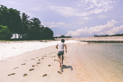 穿着白色t恤在沙滩上奔跑的男人